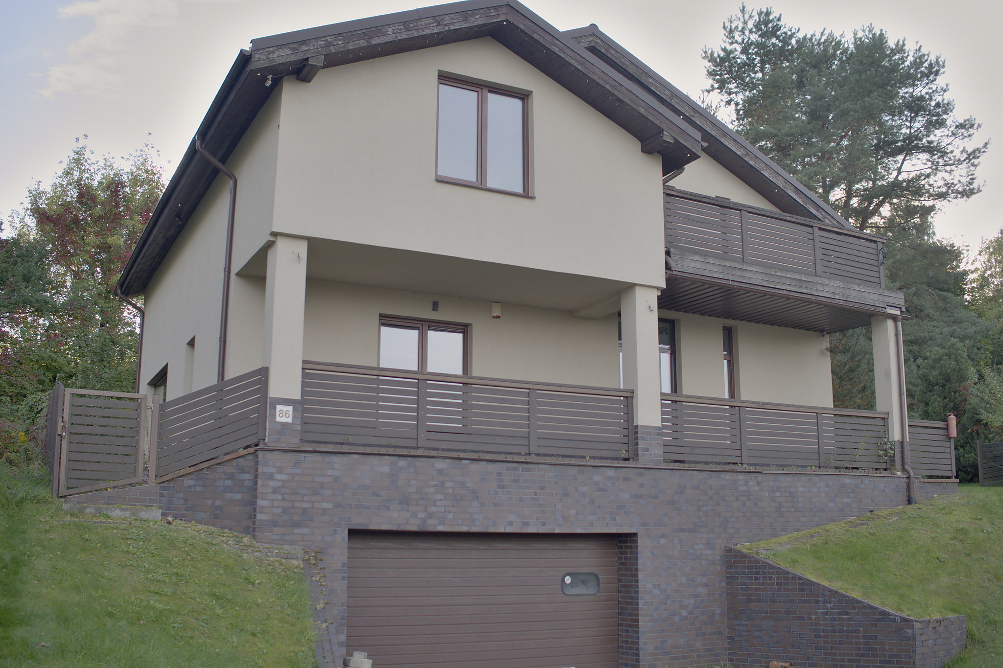 Dviejų aukštų namas su balkonu ir garažu apatiniame lygyje